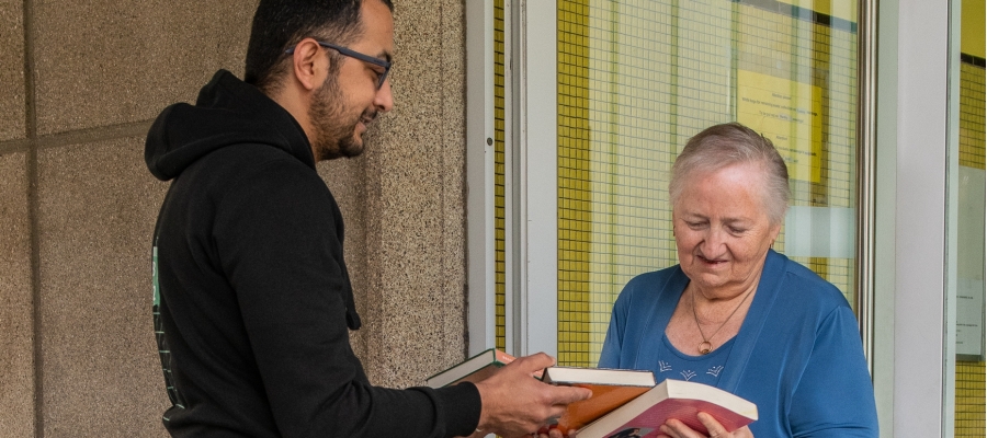 Een vrijwilliger geeft boeken af aan een oudere vrouw.